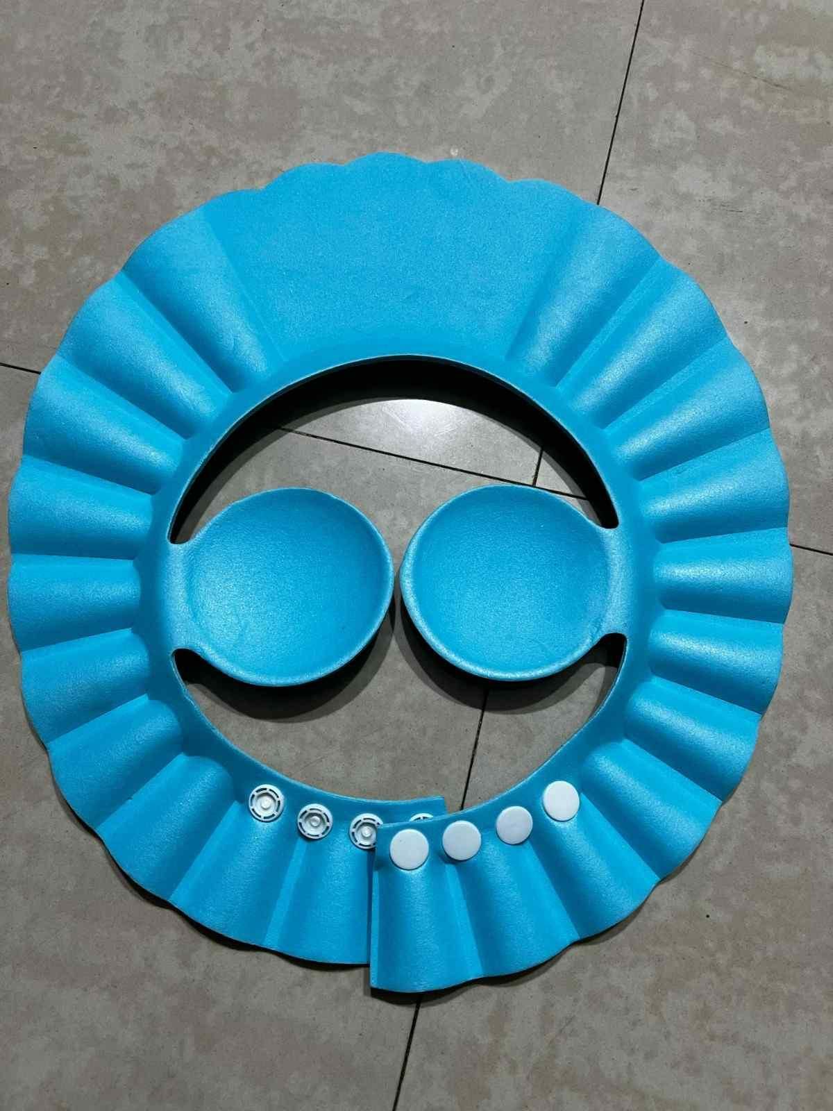 Blue plastic baby bath seat with two bowls on a tiled floor